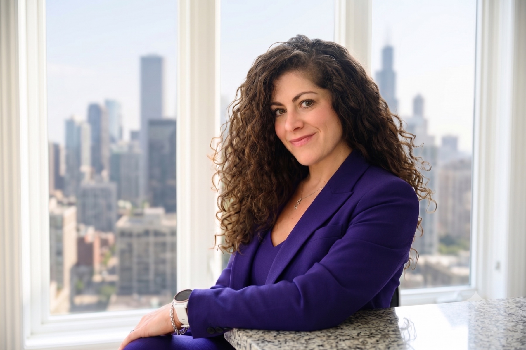 Limor Markman wearing a purple jacket in front of a city skyline